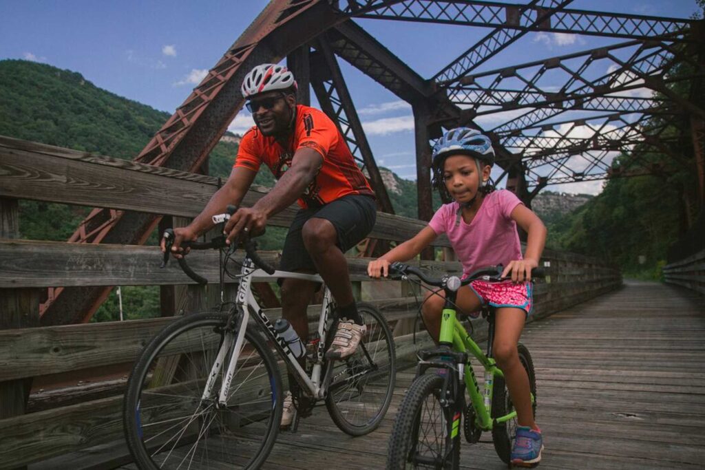 father and daughter bike riding on a wooden bridge