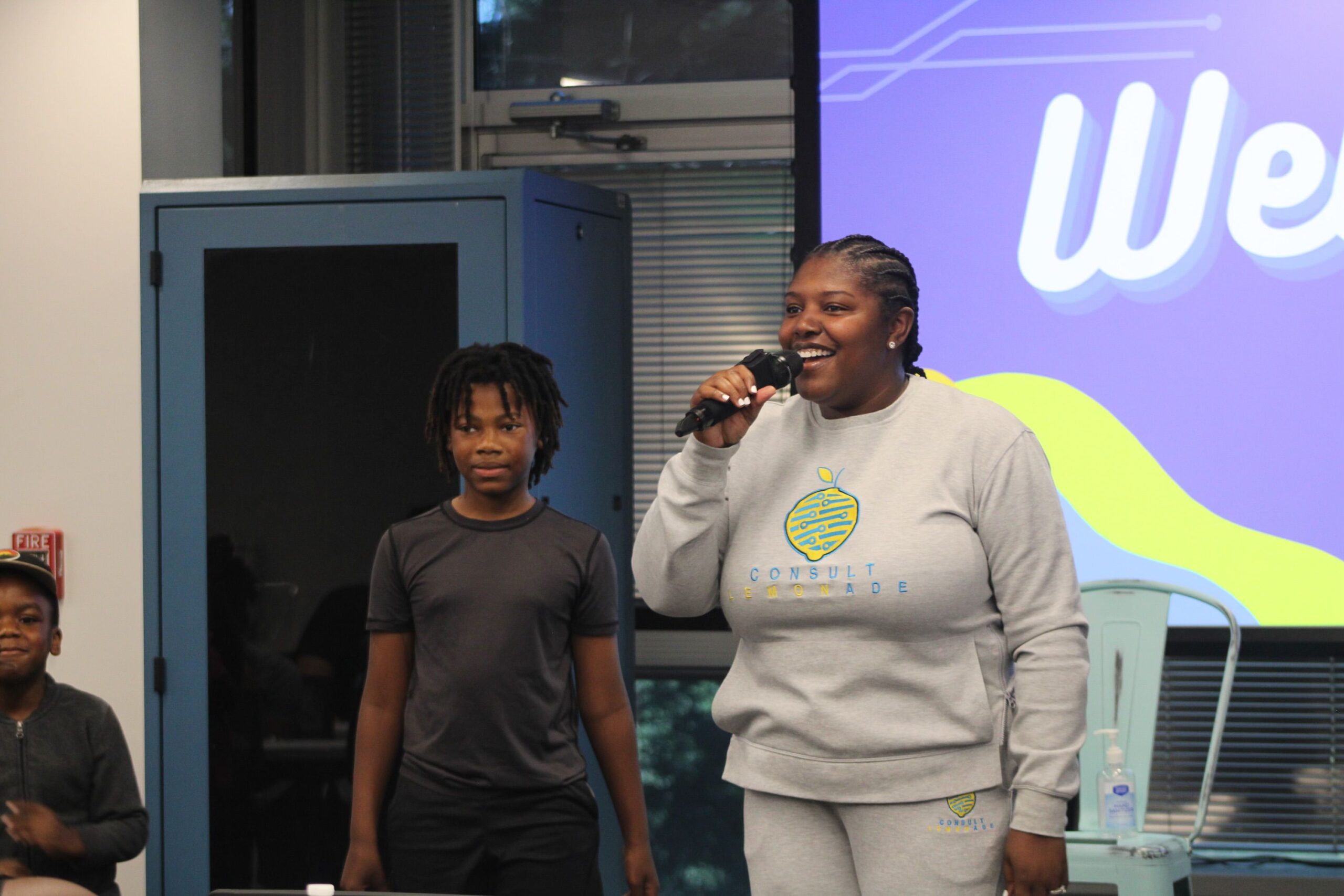 woman at at the front of room with microphone and child next to her