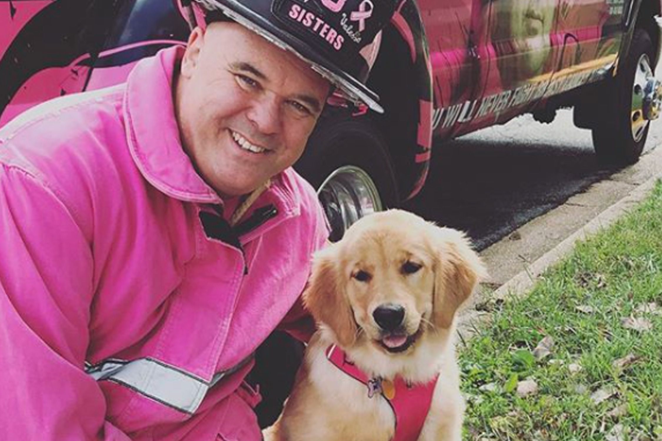 A man in a pink firefighter uniform with his golden retriever dog