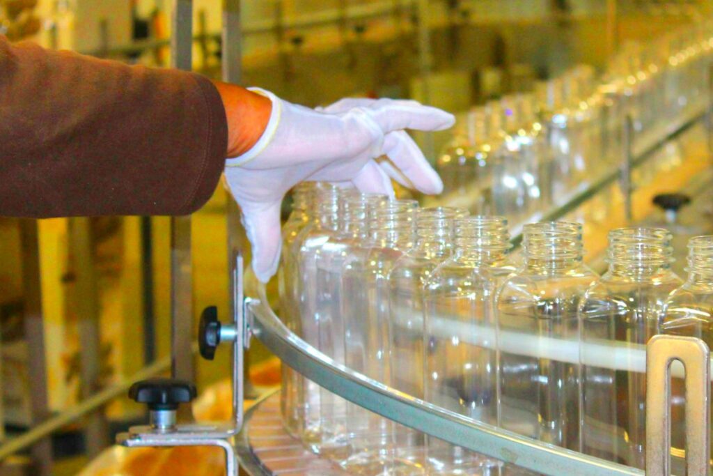 a hand covered in a rubber glove picks up bottles in a manufacturing plant