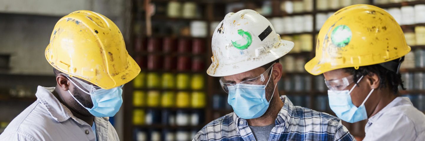Three people standing wearing hardhats and masks