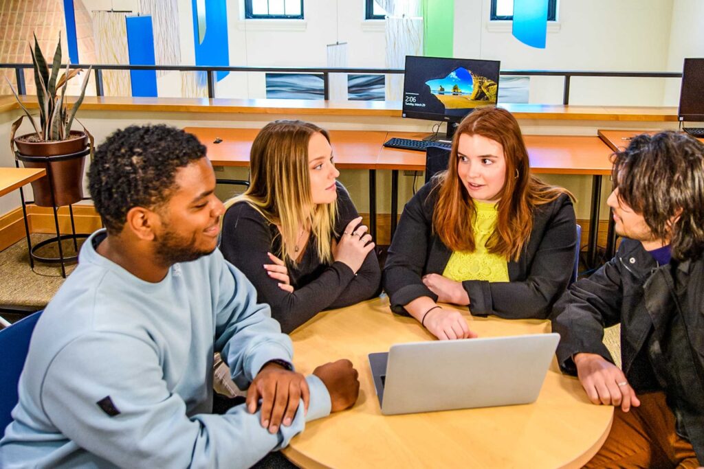 students sitting at a round table working on a laptop together