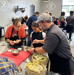 A man showing a girl and a woman how to make dumplings