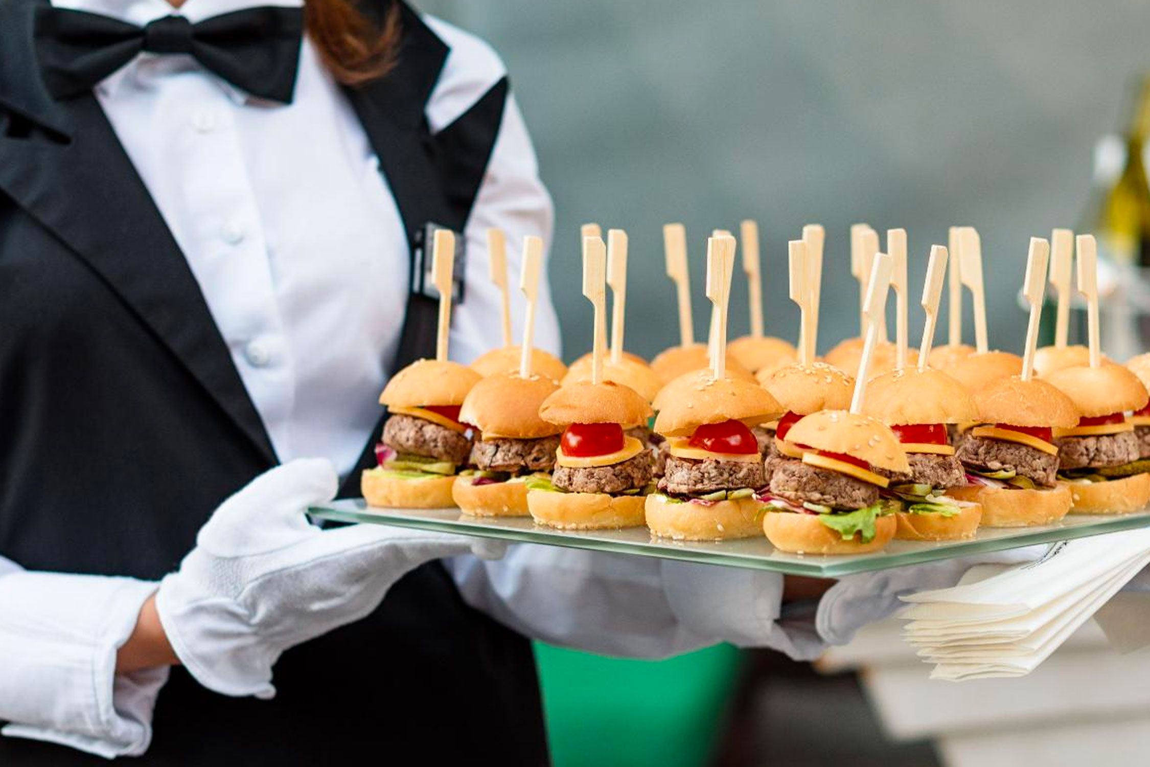 a caterer carrying a tray of mini burgers
