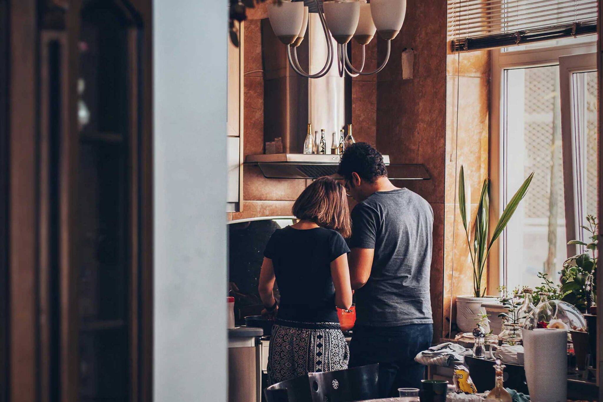 A couple stands cooking in front of a kitchen stove