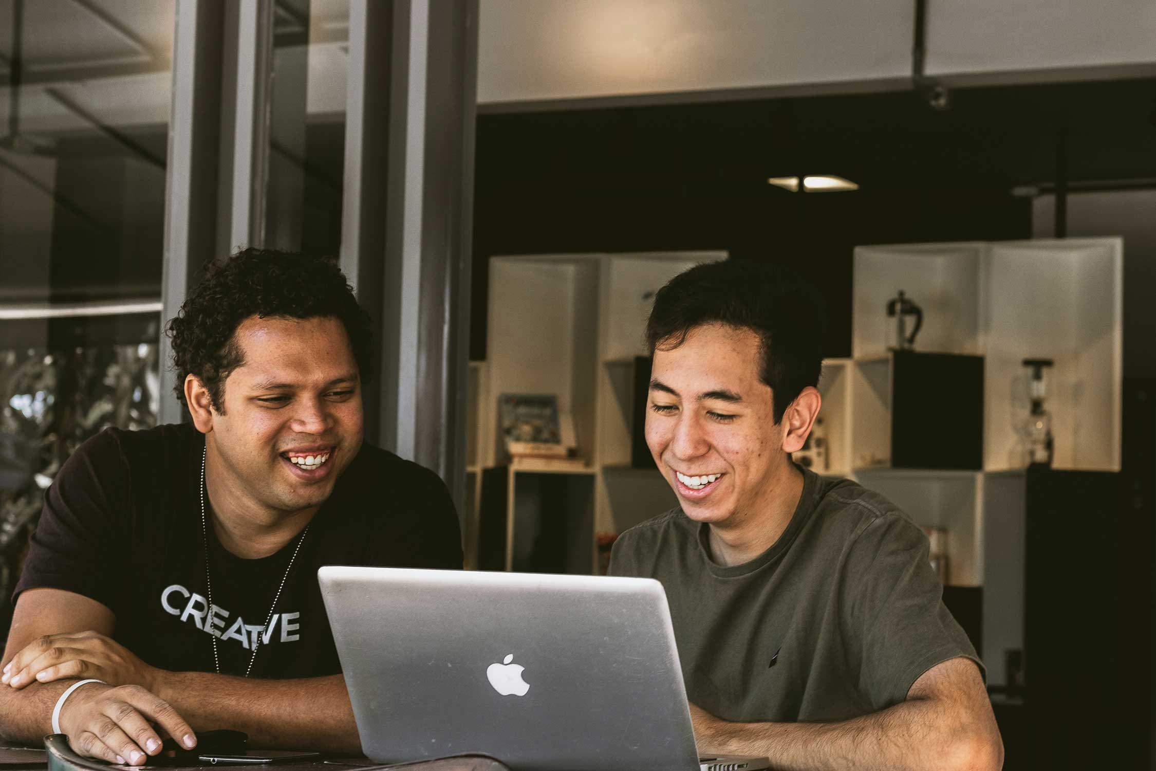 two men sitting at a table, looking at a laptop screen