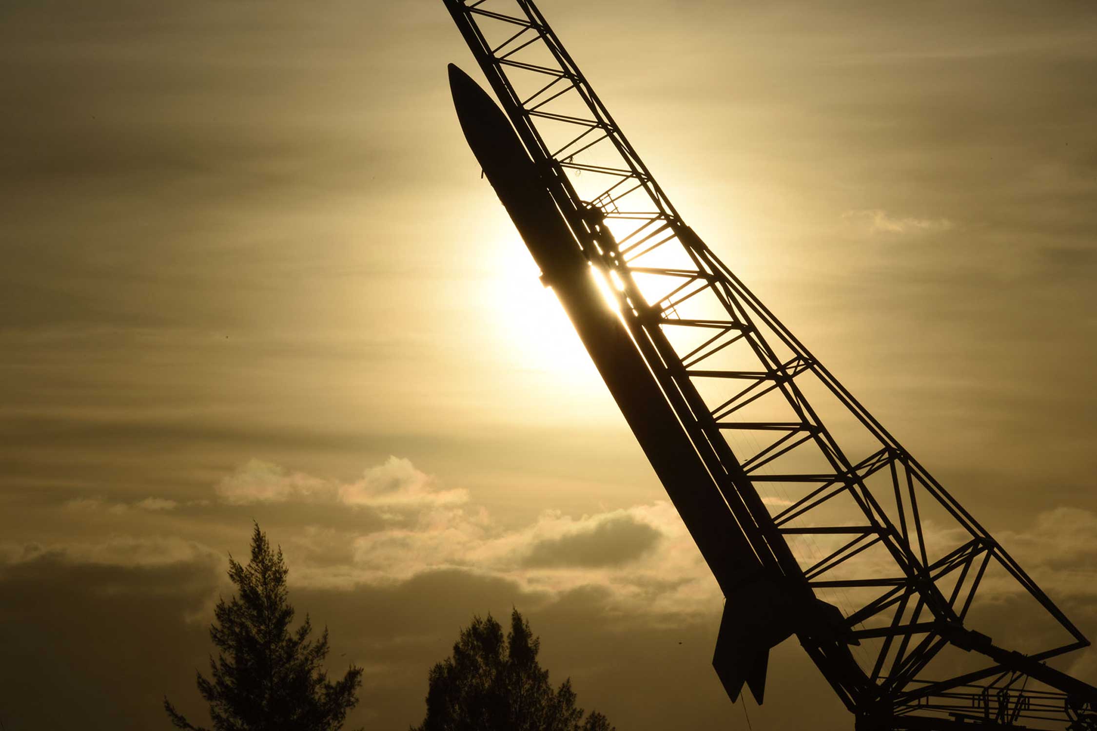 a rocket pointing towards the sky in front of a cloudy sun
