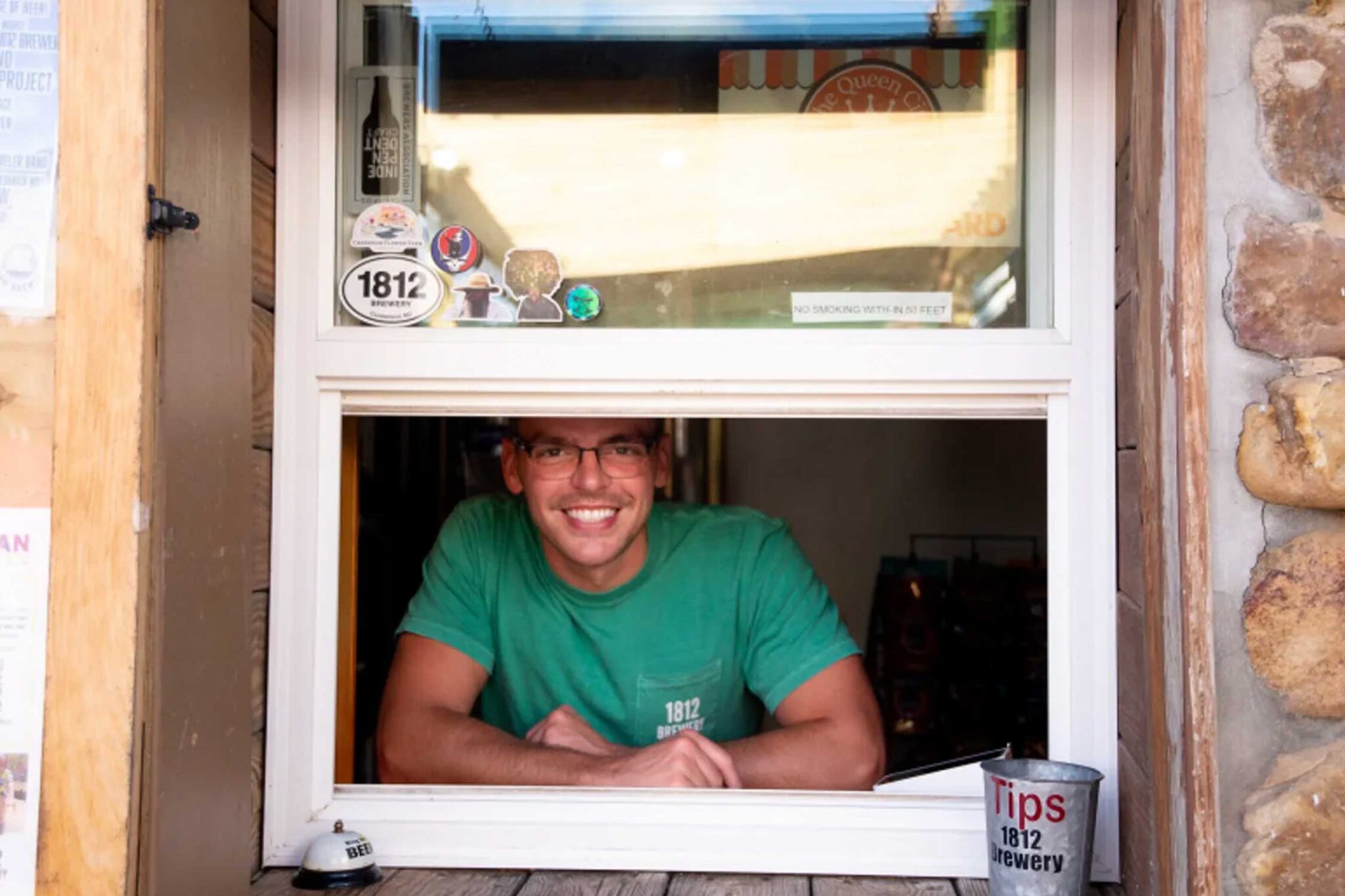 Man in a green shirt takes orders through a window at 1812 Brewery