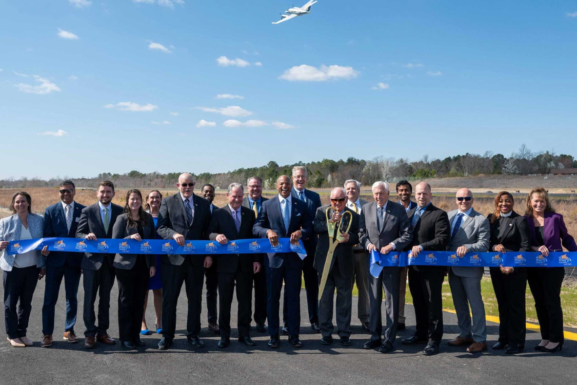 a group of individuals cut a long blue ribbon on an airport runway