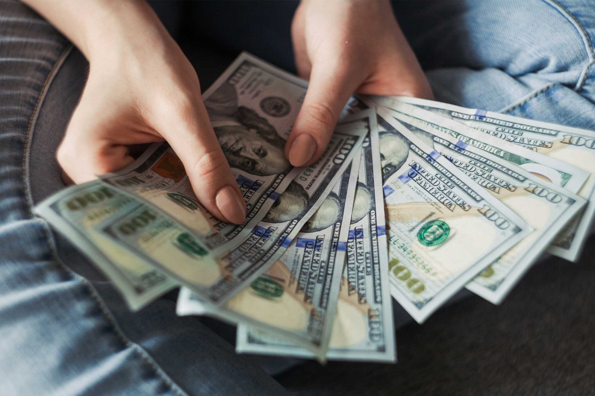 a set of hands holding multiple $100 bills