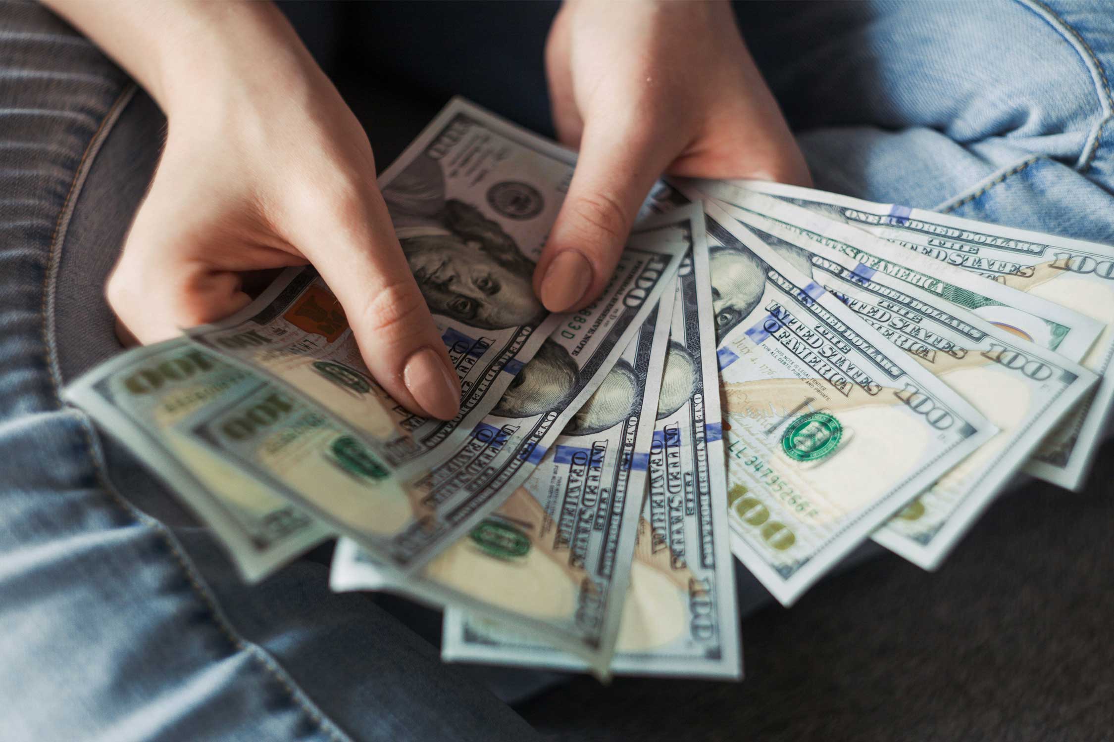 a set of hands holding multiple $100 bills