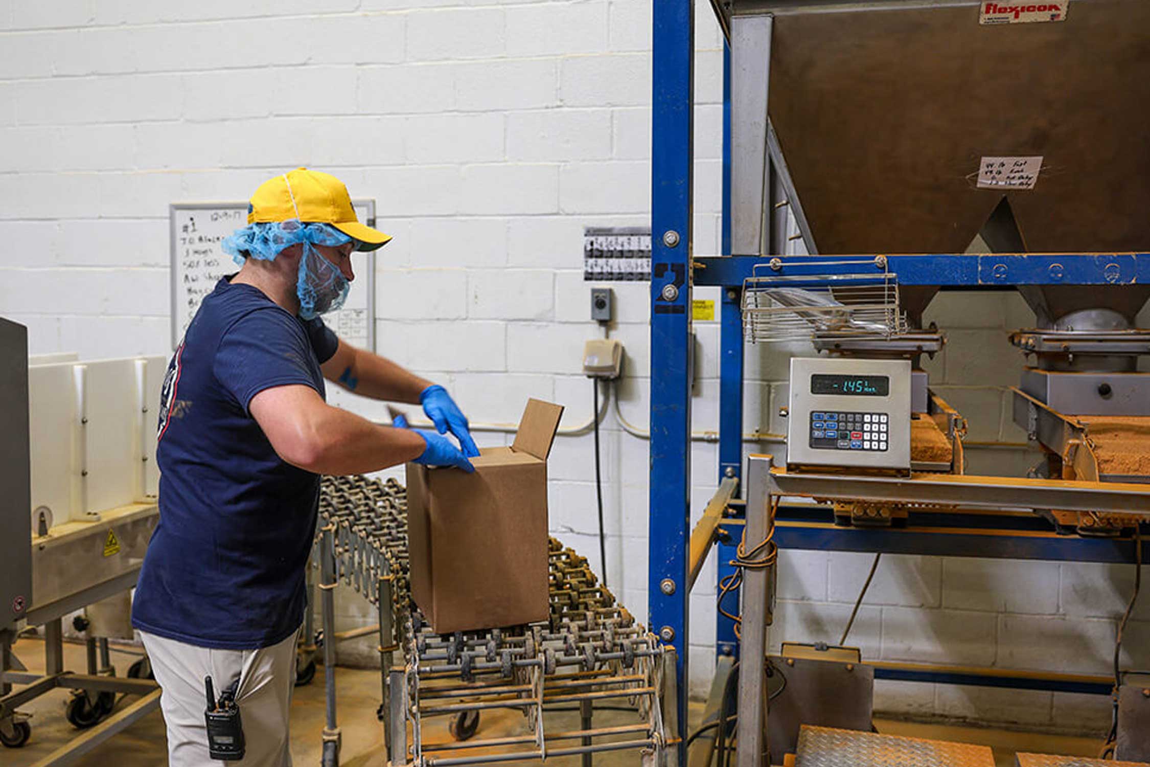 J.O. Spice Company employee packages crab seasoning at the Halethorpe warehouse, carefully filling a box beside industrial spice-blending equipment, reflecting the family-run operation’s hands-on production process