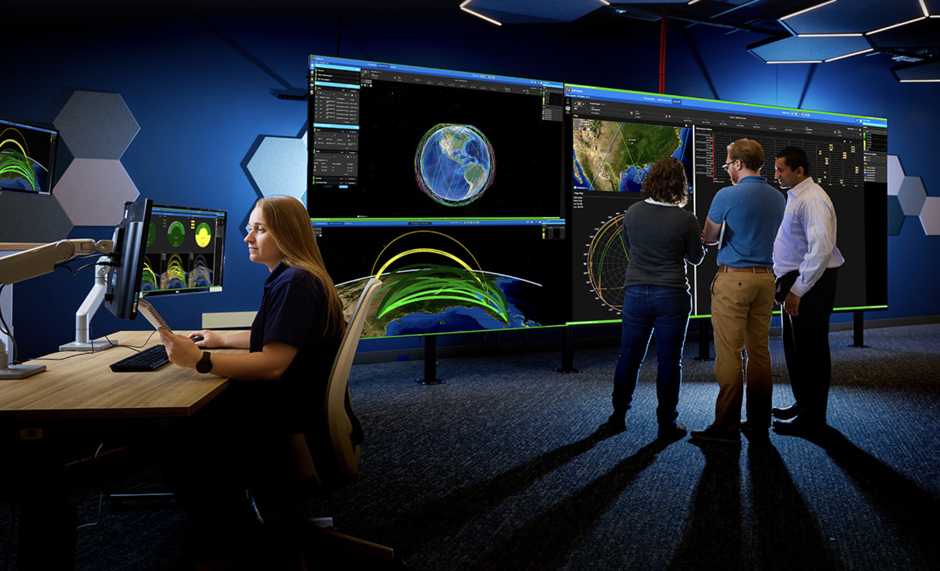 Johns Hopkins Advanced Physics Laboratory with a woman working at the desk and three people looking at a large screen that has pictures of earth